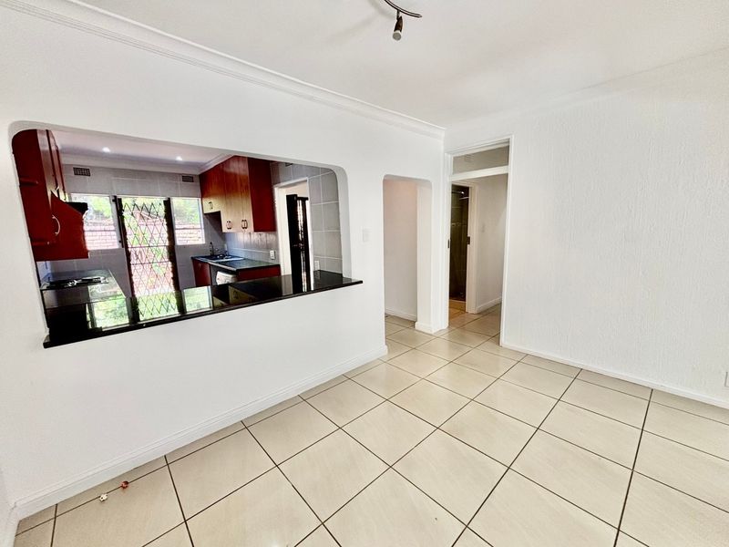 Open plan living area featuring tiled flooring and a pass-through window to the kitchen, creating a bright and functional layout.