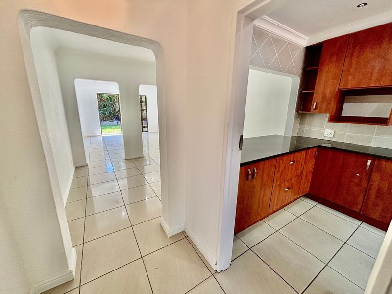 A clean kitchen featuring wooden cabinetry and dark granite countertops, with an open-plan layout leading through an archway to the living area.