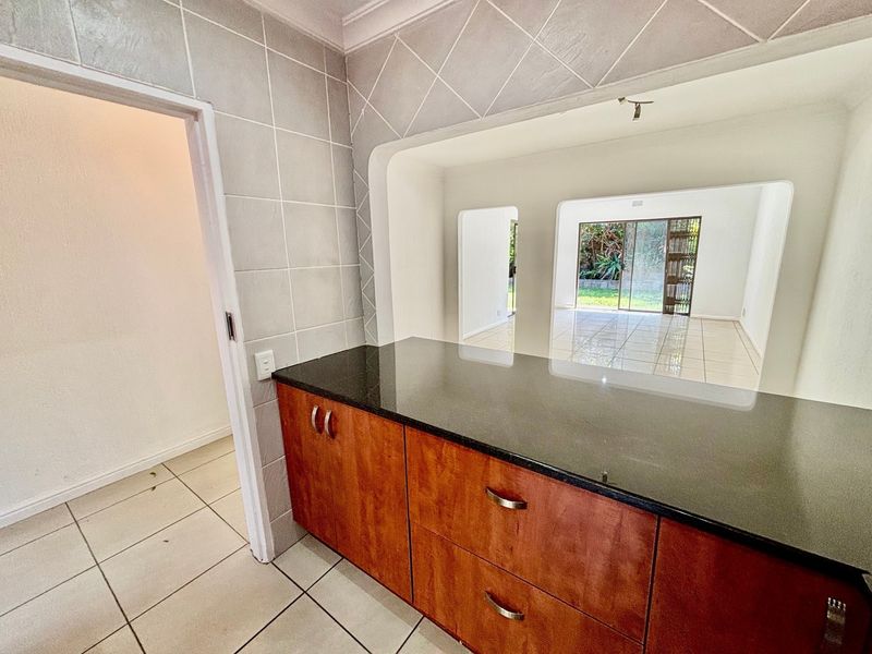 A functional kitchen area featuring dark granite countertops, wooden cabinetry, and tiled flooring, with an open-plan layout looking through to the living space.