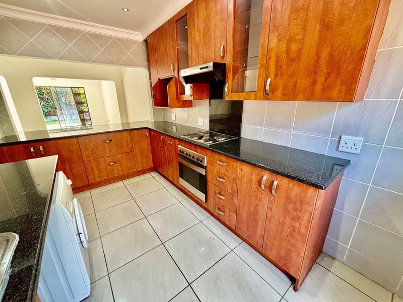 A functional kitchen featuring wooden cabinetry, granite countertops, a built-in oven with hob, and tiled flooring, offering a clean and practical workspace.