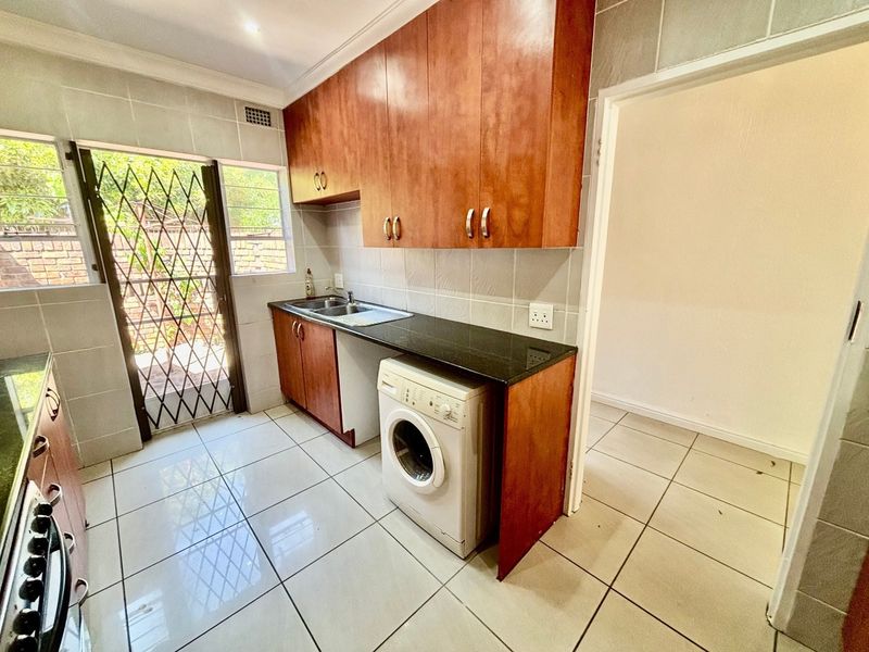 Functional kitchen featuring wood-finish cabinetry, granite countertops, tiled flooring, and direct access to the exterior via a security gate.