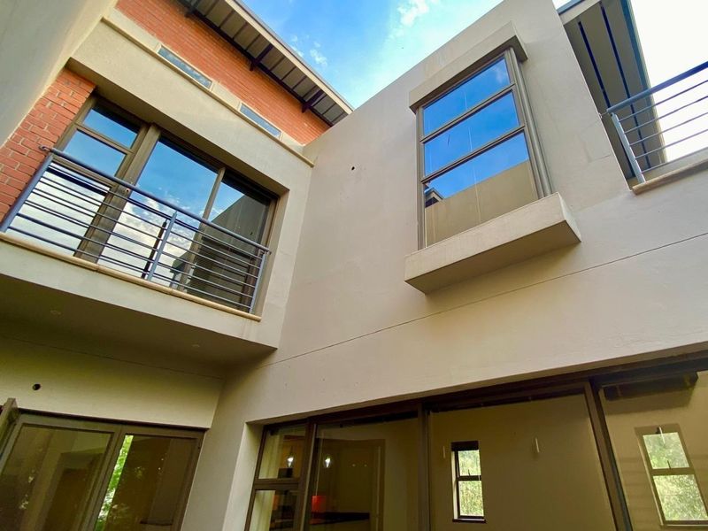 A view of the rear exterior facade featuring modern architectural design, large aluminium windows, and a balcony with metal railings.