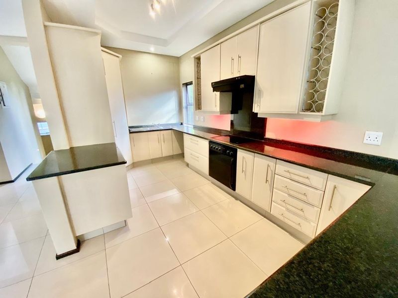 Modern kitchen featuring white cabinetry, dark granite countertops, integrated stove with extractor fan, and tiled flooring in a clean, open layout.