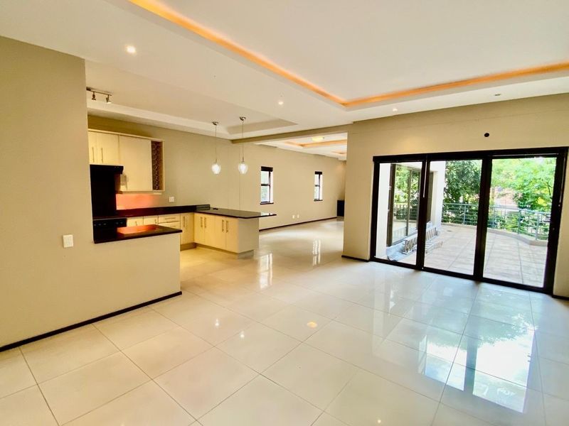 Spacious open-plan living and kitchen area featuring modern tiled floors, recessed ceiling lighting, and large sliding doors leading to an outdoor patio.