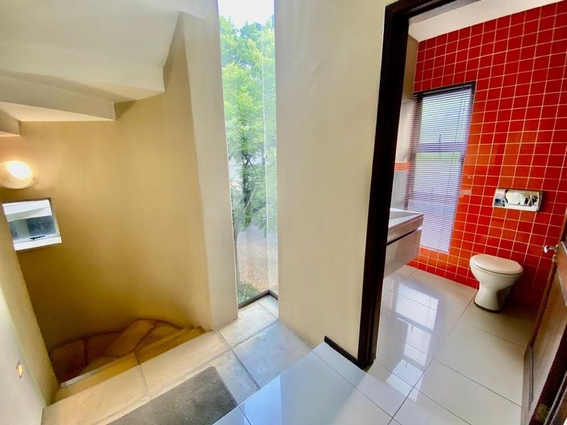 A bathroom featuring a wall-mounted toilet and vanity, adjacent to a staircase with a large floor-to-ceiling window providing natural light.