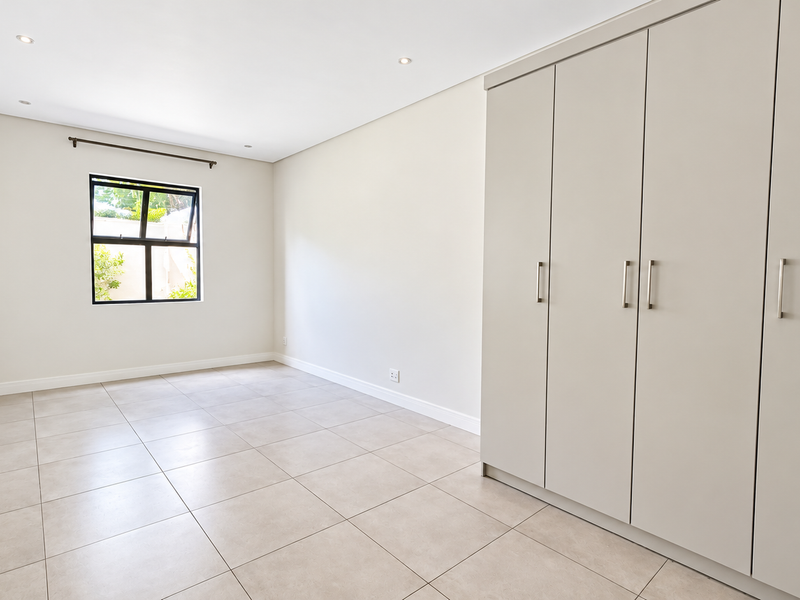 A bright and spacious bedroom featuring neutral tiled flooring, recessed downlights, and ample built-in cupboard storage.