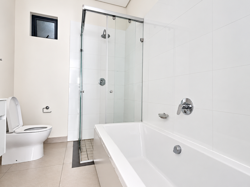 A modern, clean bathroom featuring a glass-enclosed shower, a white bathtub, a wall-mounted vanity, and a toilet with neutral floor and wall tiling.