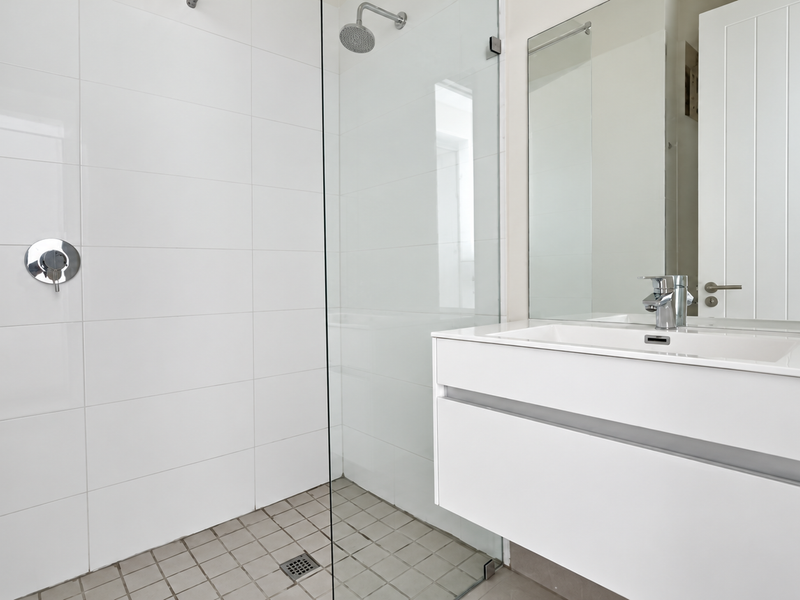 Modern bathroom featuring a spacious walk-in shower with glass screen, floating vanity with integrated basin, and clean white wall tiling.