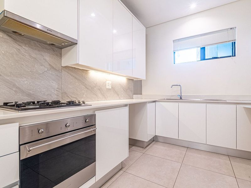 Modern kitchen featuring sleek white cabinetry, stone countertops, integrated gas hob, oven, and extractor fan with neutral tiled flooring.