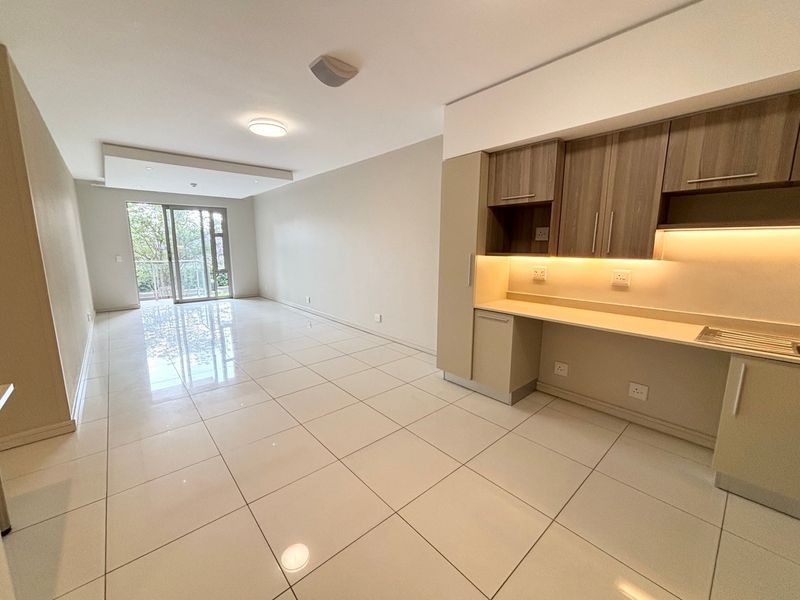 Modern open-plan living area featuring sleek tiled floors, built-in kitchen cabinetry with under-cabinet lighting, and a sliding glass door leading to a balcony.