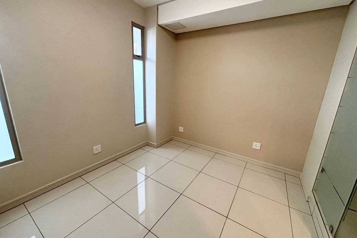 A clean, empty bedroom featuring neutral wall paint, polished floor tiles, and a vertical window, providing a blank canvas for interior design.