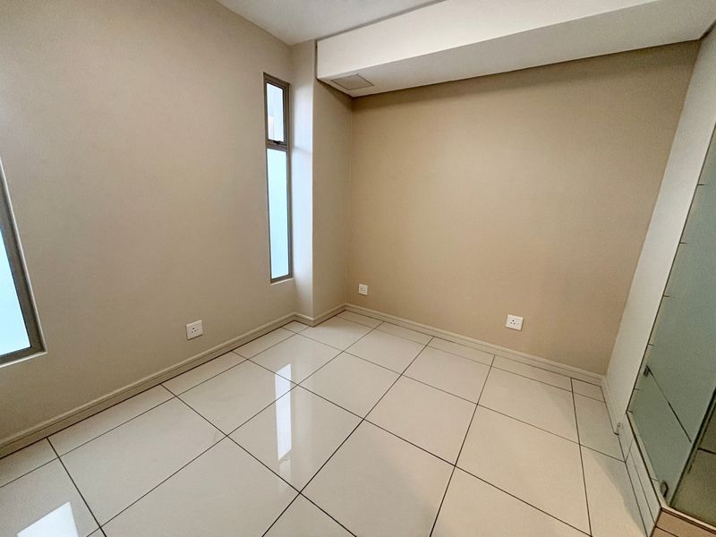 A clean, empty bedroom featuring neutral wall paint, polished floor tiles, and a vertical window, providing a blank canvas for interior design.
