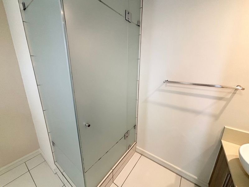 A clean bathroom featuring a frosted glass shower enclosure, tiled flooring, a wall-mounted towel rail, and a built-in vanity basin.