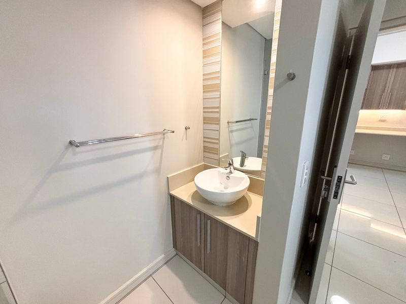 A modern guest bathroom featuring a vessel sink, vanity cabinet, and wall-mounted mirror with neutral tiled flooring.
