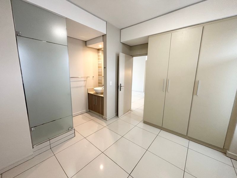 A clean, modern bedroom featuring built-in cupboards, tiled flooring, and an integrated vanity area with a basin and frosted glass partition.