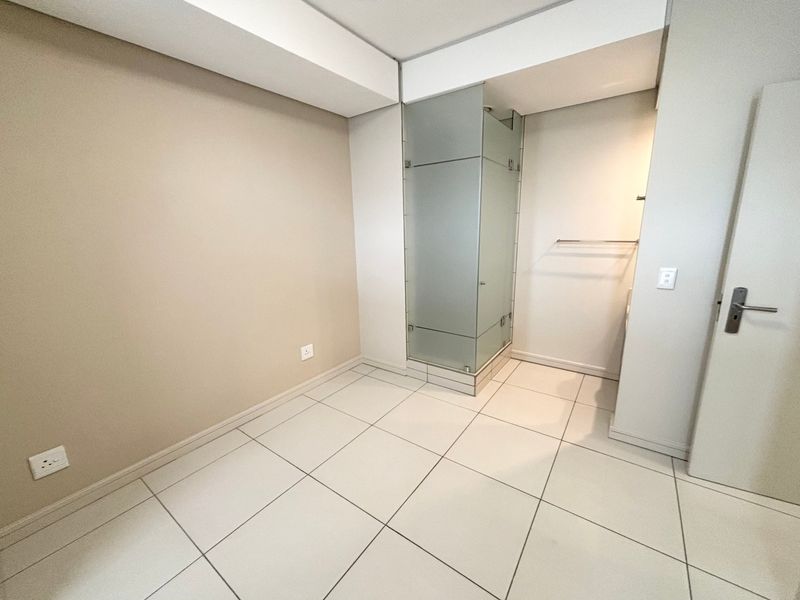 A clean, modern bathroom featuring a frosted glass shower enclosure and neutral tiled flooring, presenting a bright and well-maintained space.