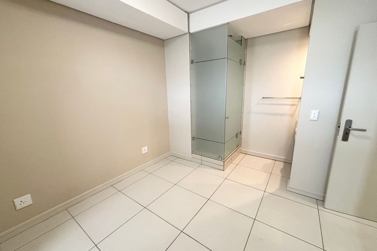 A clean, modern bathroom featuring a frosted glass shower enclosure and neutral tiled flooring, presenting a bright and well-maintained space.