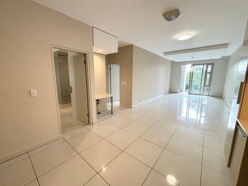 Spacious open-plan living area featuring polished porcelain floor tiles, recessed ceiling lighting, and direct access to a balcony through sliding glass doors.