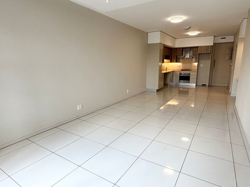 An open-plan living and kitchen area featuring polished tiled flooring, modern built-in cabinetry, and integrated kitchen appliances in a clean, neutral space.