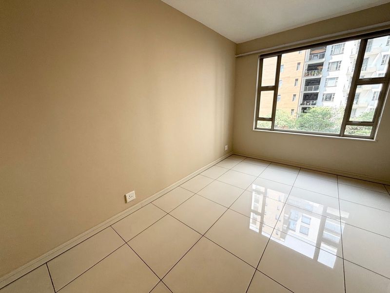 A bright, empty bedroom featuring neutral wall paint, large aluminium-framed windows, and clean tiled flooring throughout.
