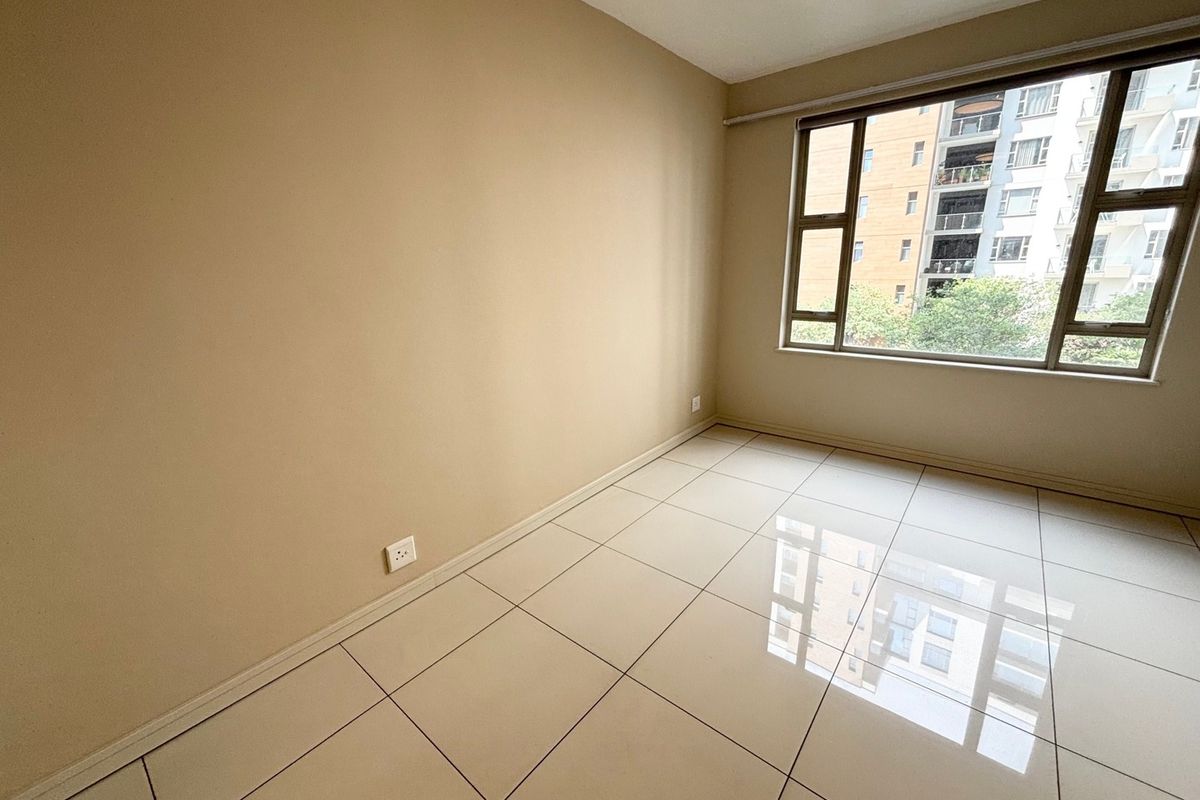 A bright, empty bedroom featuring neutral wall paint, large aluminium-framed windows, and clean tiled flooring throughout.