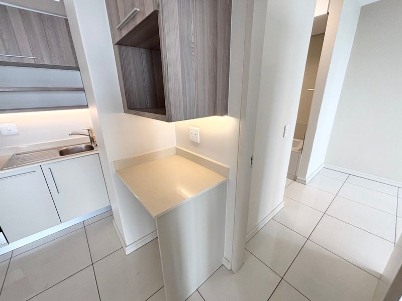 Modern kitchen area featuring sleek built-in cabinetry, stone countertops, stainless steel sink, and integrated under-cabinet lighting with clean tiled flooring throughout.