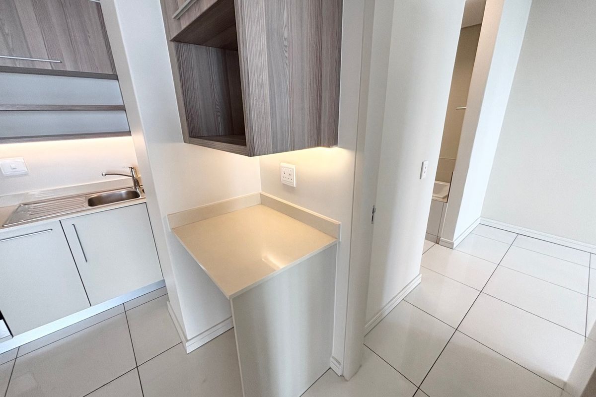 Modern kitchen area featuring sleek built-in cabinetry, stone countertops, stainless steel sink, and integrated under-cabinet lighting with clean tiled flooring throughout.