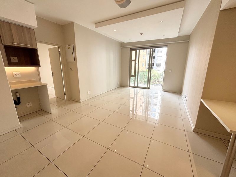 A bright, open-plan living area featuring polished tile flooring, recessed ceiling lights, and a sliding glass door leading to a balcony.