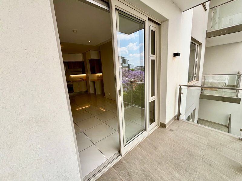 A modern balcony with glass balustrades and tiled flooring, providing seamless access to the open-plan interior living and kitchen area.