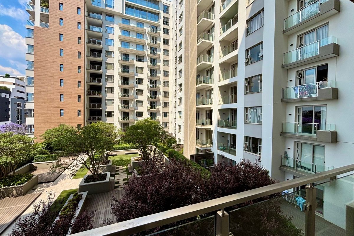 A view of a modern apartment complex featuring a well-maintained landscaped courtyard with timber decking, raised planters, and glass-balustraded balconies.