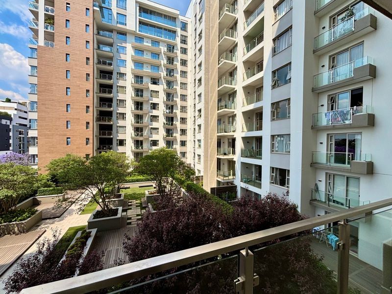 A view of a modern apartment complex featuring a well-maintained landscaped courtyard with timber decking, raised planters, and glass-balustraded balconies.