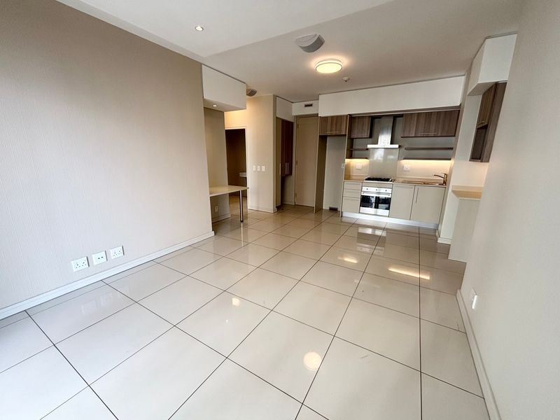 Modern open-plan living area featuring large format floor tiles, recessed lighting, and a compact kitchen with built-in appliances and cabinetry.