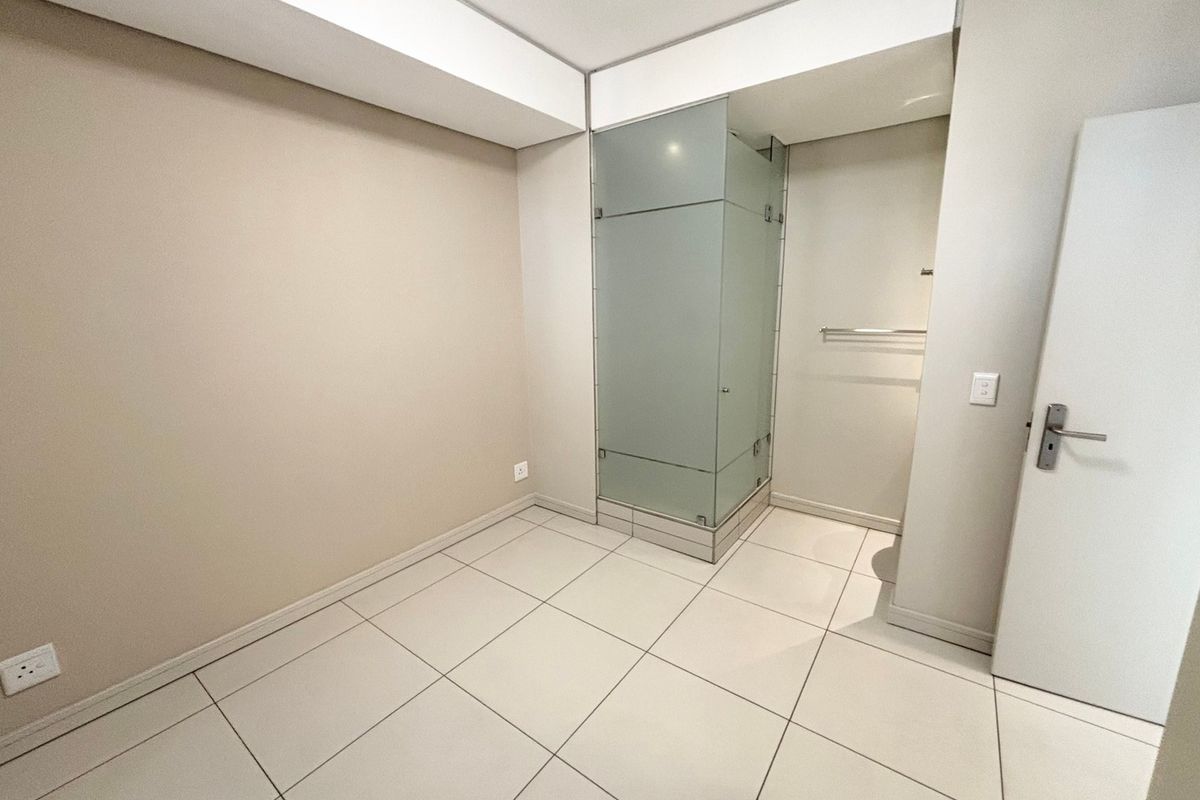A clean, modern bathroom featuring a frosted glass shower enclosure, neutral tiled flooring, and a minimalist design with a recessed ceiling bulkhead.