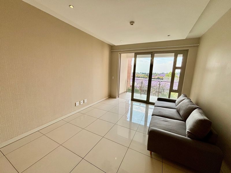 A bright living room featuring neutral textured wallpaper, large format floor tiles, and a sliding glass door leading to a private balcony.