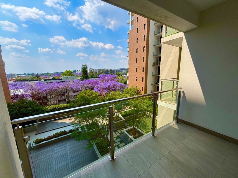 A modern balcony featuring a sleek glass balustrade with stainless steel railings, offering elevated views over the surrounding landscaped gardens and neighbourhood.