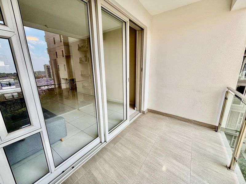 A clean, modern balcony featuring tiled flooring, a glass balustrade, and large sliding glass doors providing access to the interior living space.