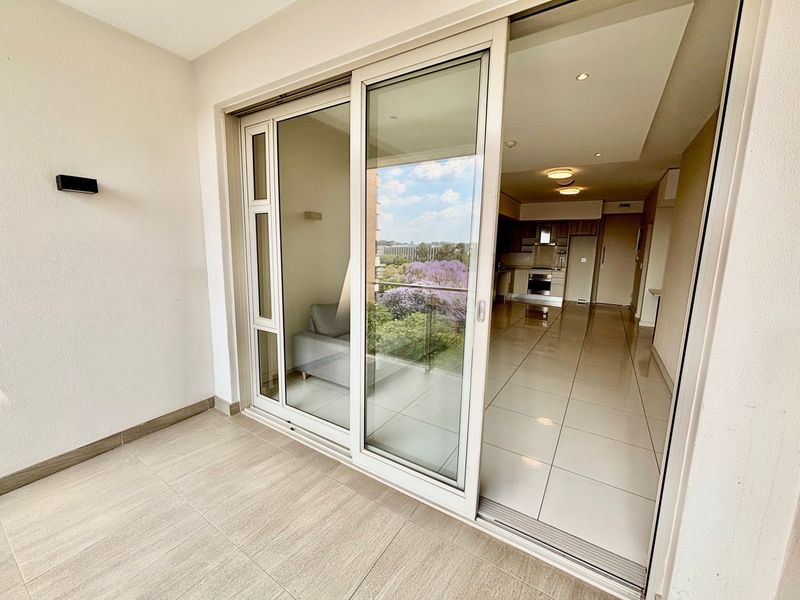A covered balcony with tiled flooring and large sliding glass doors providing a seamless transition into the open-plan kitchen and living area.