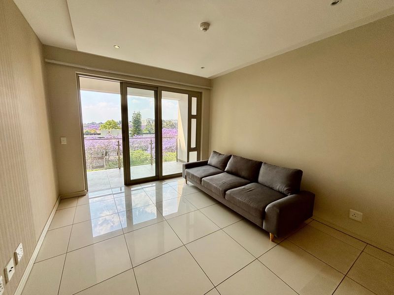 Bright living room featuring large sliding glass doors leading to a balcony with scenic views, complemented by neutral tiled flooring and recessed ceiling lights.