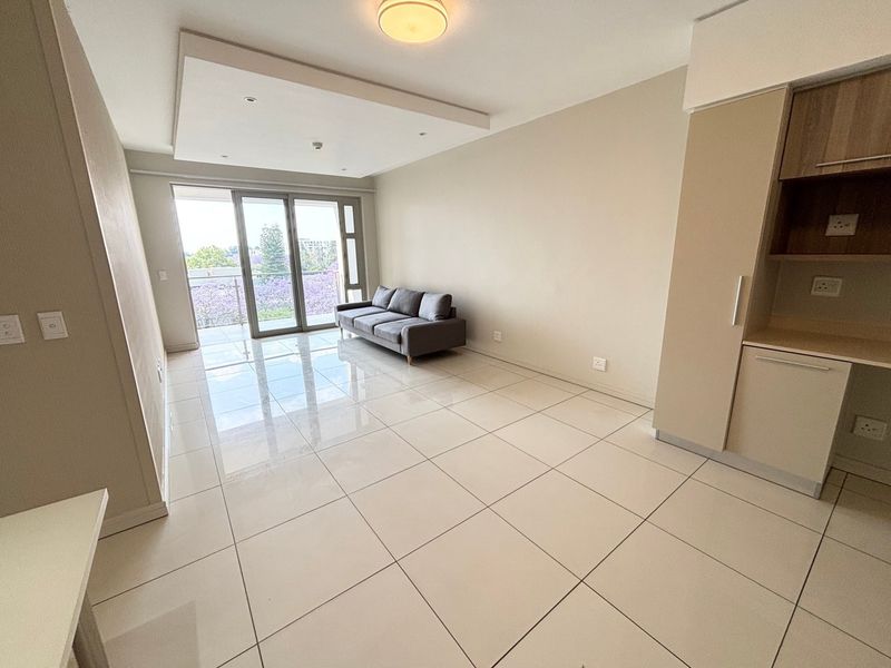 Modern open-plan living area featuring large format floor tiles, recessed ceiling lighting, and a sliding door leading to a private balcony.