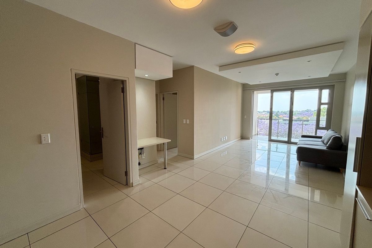 Spacious open-plan living area featuring polished tile flooring, recessed lighting, and large sliding doors leading to a balcony with scenic views.
