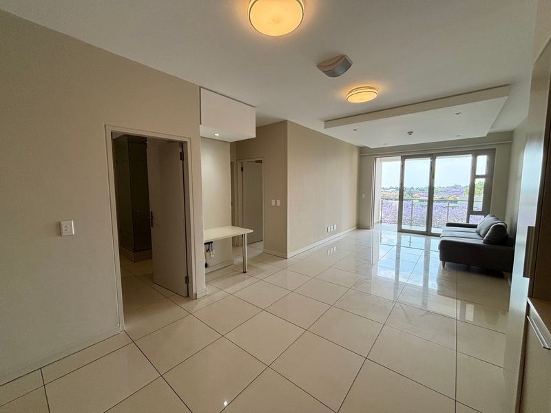 Spacious open-plan living area featuring polished tile flooring, recessed lighting, and large sliding doors leading to a balcony with scenic views.