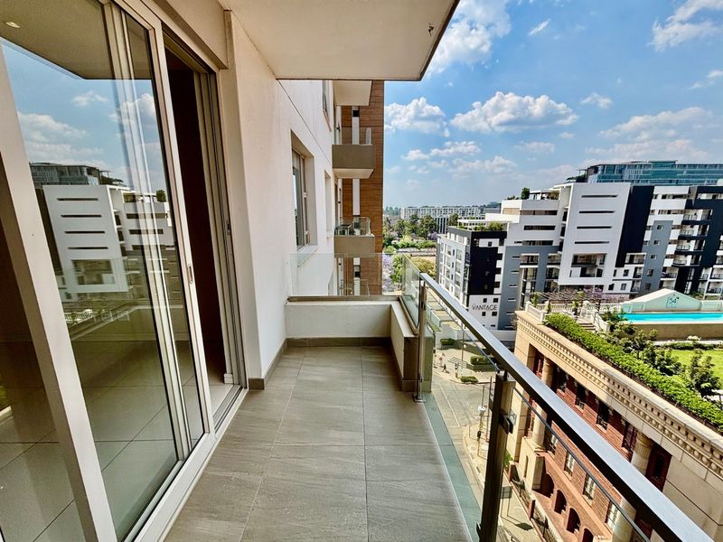 A modern apartment balcony featuring tiled flooring and a sleek glass balustrade, offering an elevated view of the surrounding urban landscape.