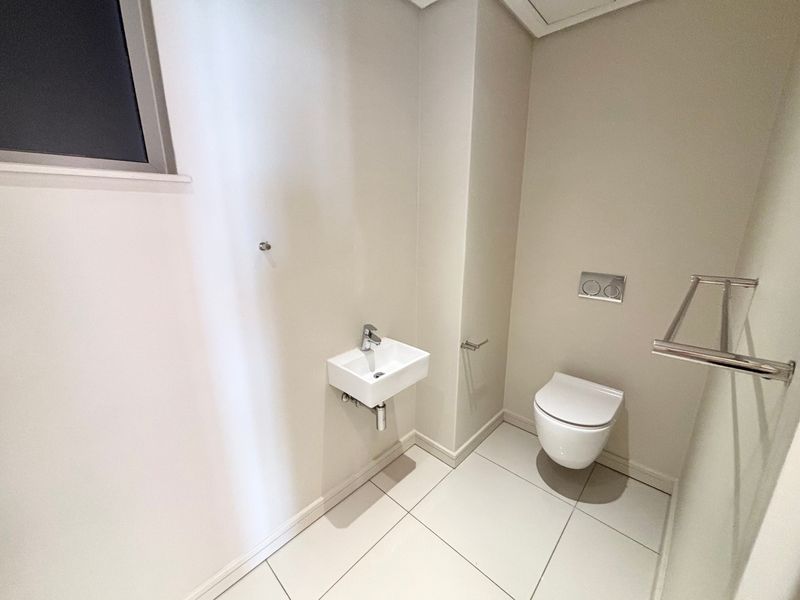A modern, minimalist guest bathroom featuring a wall-hung toilet with a concealed cistern, a compact wall-mounted basin, and clean tiled flooring.