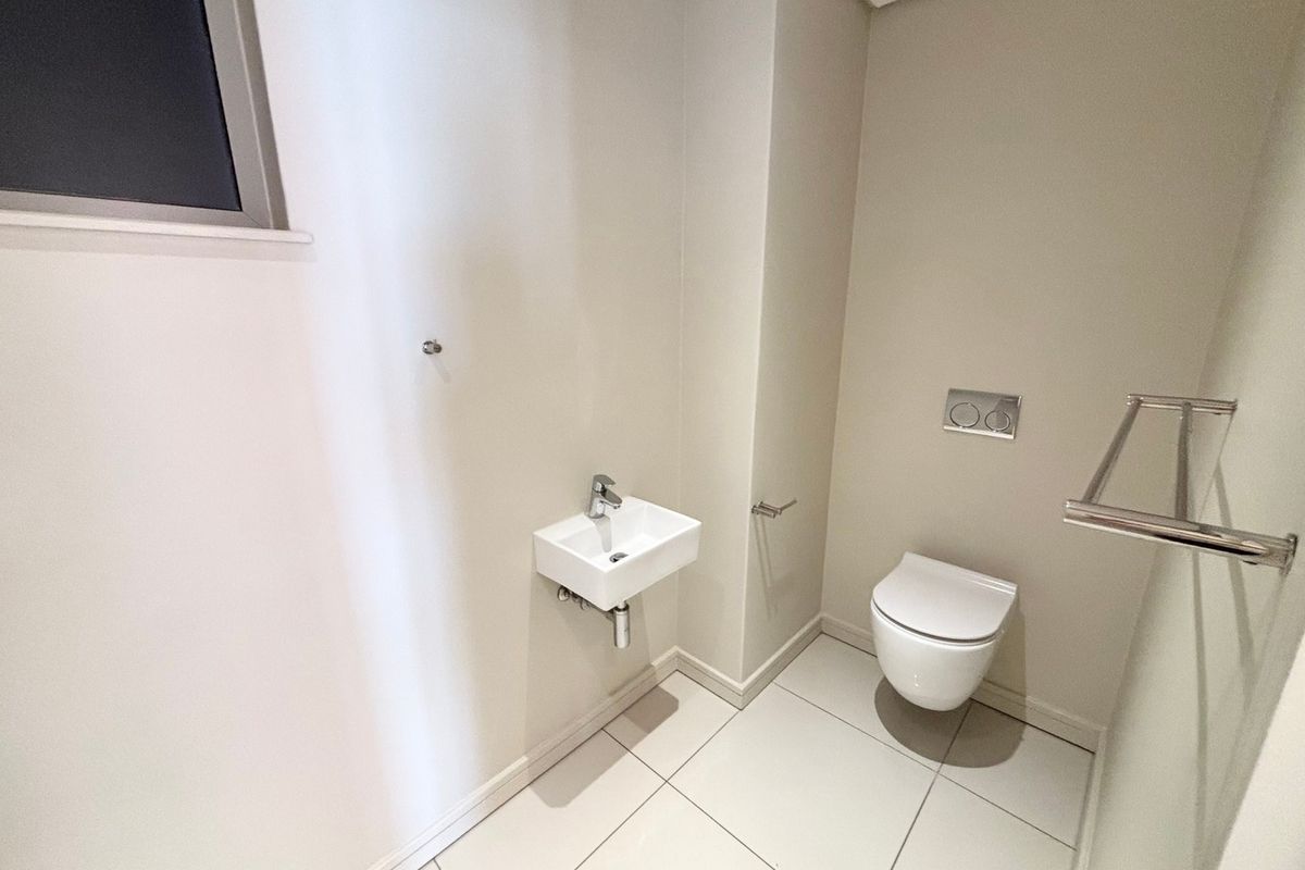 A modern, minimalist guest bathroom featuring a wall-hung toilet with a concealed cistern, a compact wall-mounted basin, and clean tiled flooring.