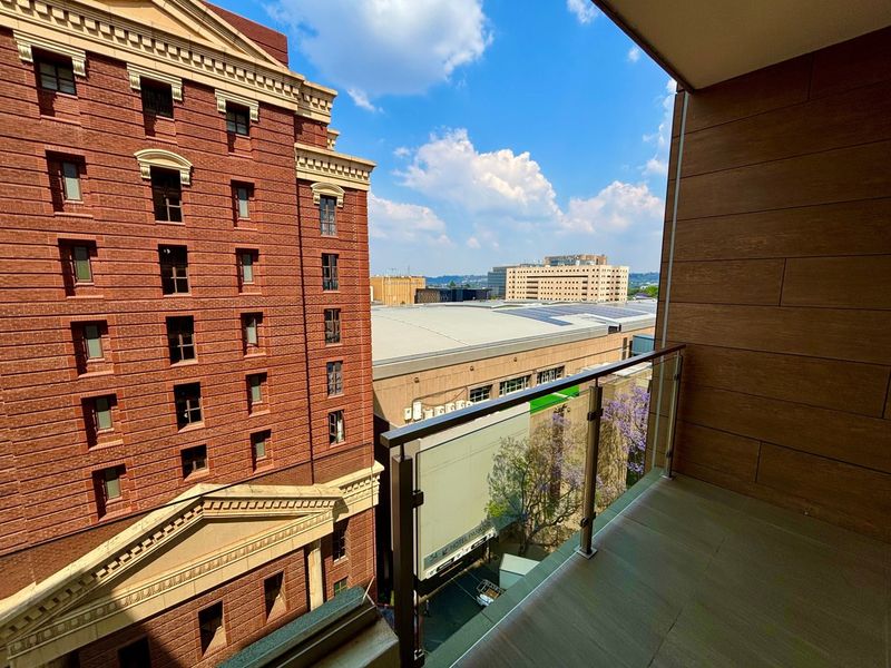 A modern balcony featuring a glass balustrade, tiled flooring, and wood-look wall cladding, offering an urban city view.
