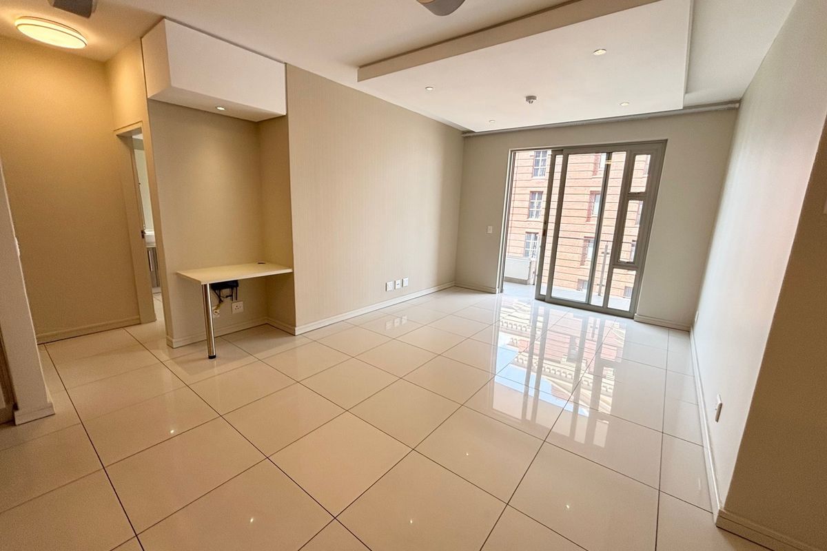 A bright, open-plan living area featuring polished tile flooring, a modern bulkhead ceiling with recessed lighting, and a built-in desk space.