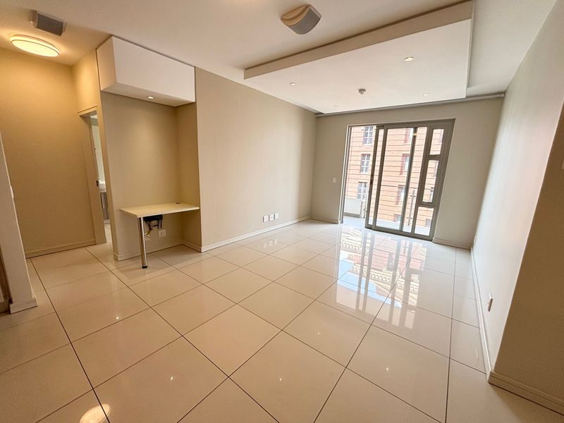A bright, open-plan living area featuring polished tile flooring, a modern bulkhead ceiling with recessed lighting, and a built-in desk space.
