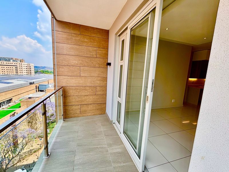 A modern balcony featuring a glass balustrade, wood-look wall cladding, and tiled flooring, providing a seamless transition to the interior living space.