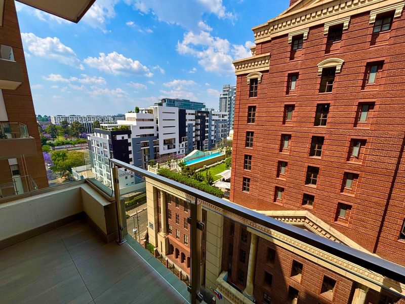 A modern balcony featuring a glass balustrade and tiled flooring, offering an elevated urban view of the surrounding apartment complex and cityscape.