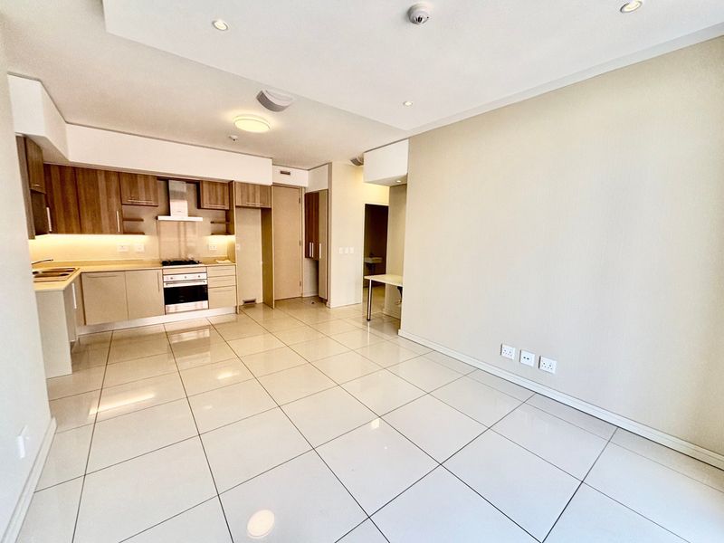 An open-plan living and kitchen area featuring modern cabinetry, integrated appliances, tiled flooring, and recessed lighting in a clean, vacant space.